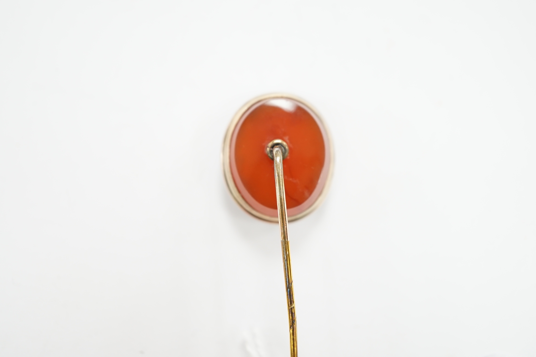 An early 20th century yellow metal and oval intaglio chalcedony set stick pin, 77mm.